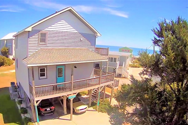 Coastal retreat with elevated beach house design, covered parking, and multiple decks surrounded by natural dunes and sea oats.