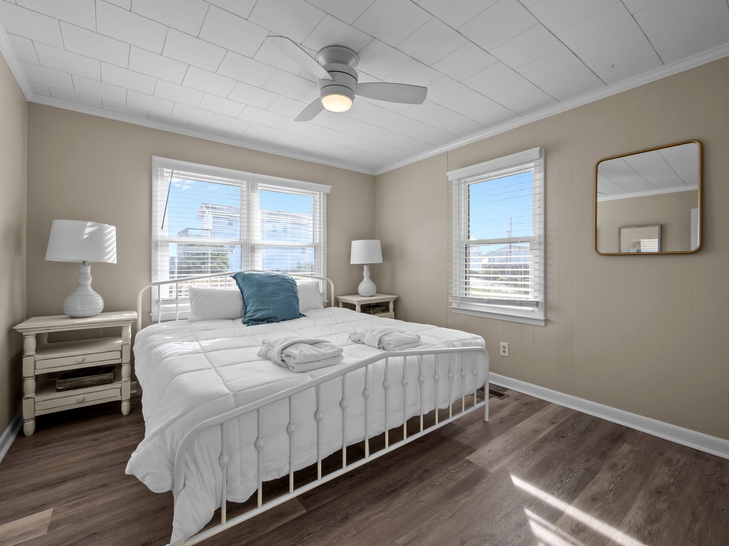 Your peaceful bedroom features fresh white linens and city views through two bright windows. The ceiling fan ensures comfort while you rest.