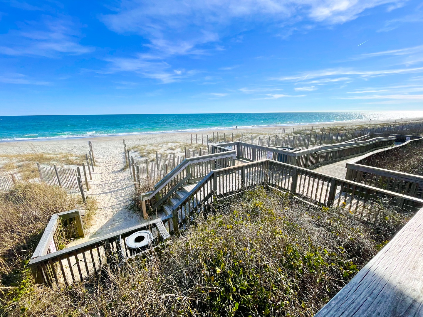 Pristine coastline with wooden walkways leading to expansive sandy shores and crystal-clear waters under brilliant blue skies.