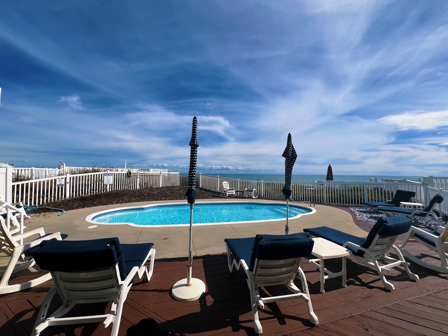 Rooftop pool deck offers panoramic ocean views with comfortable loungers and tables under expansive blue skies.
