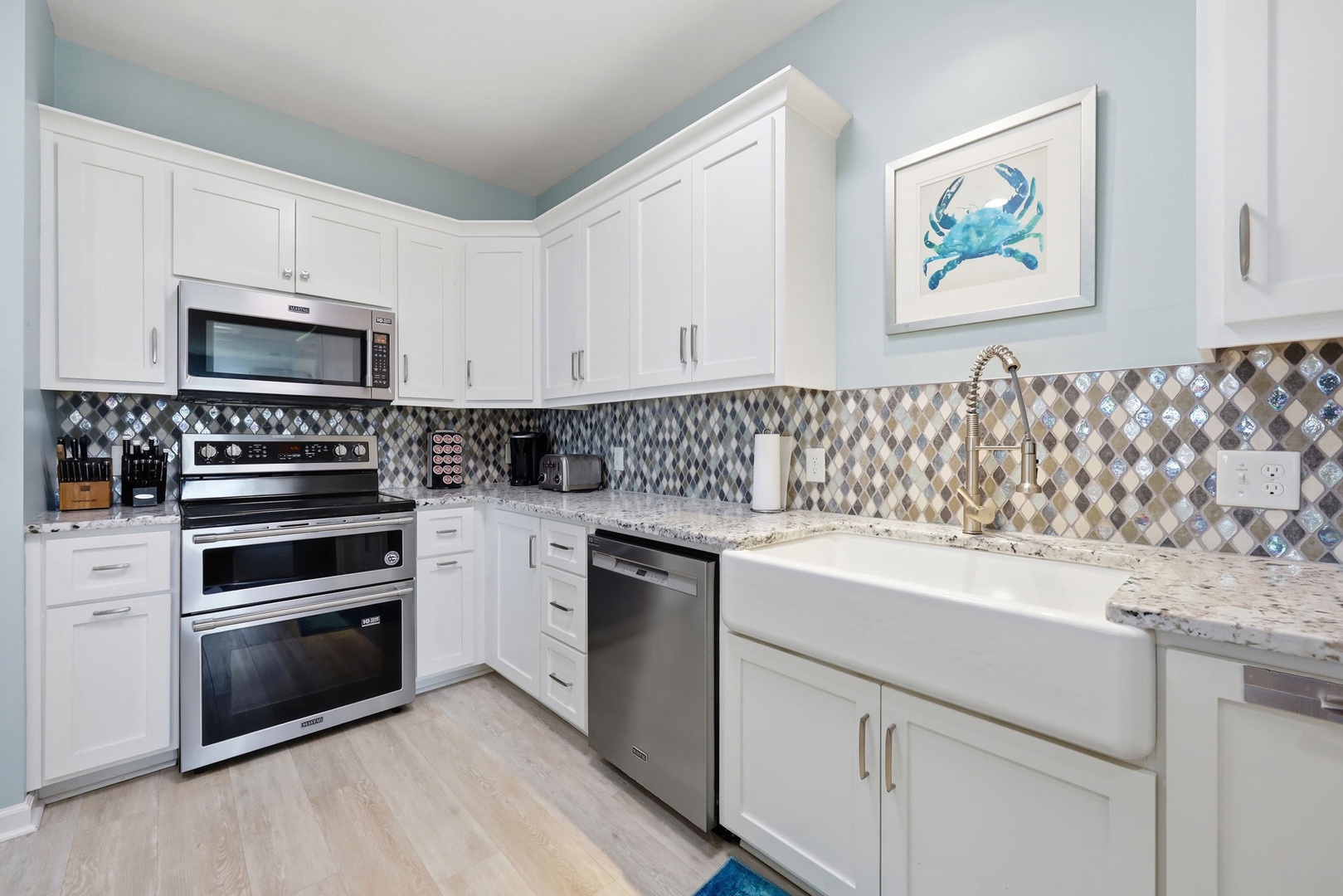 Your fully equipped kitchen features gleaming white cabinetry, modern stainless appliances, and a charming coastal crab accent—perfect for preparing delicious vacation meals together.