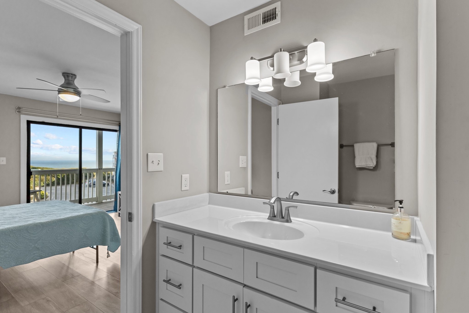 Your bright bathroom features modern lighting, ample counter space, and a view into the bedroom with ocean glimpses beyond.