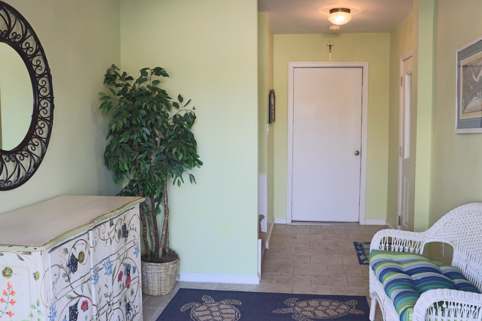 Step into your bright, welcoming entryway where soft green walls and charming wicker furniture create the perfect coastal retreat atmosphere.