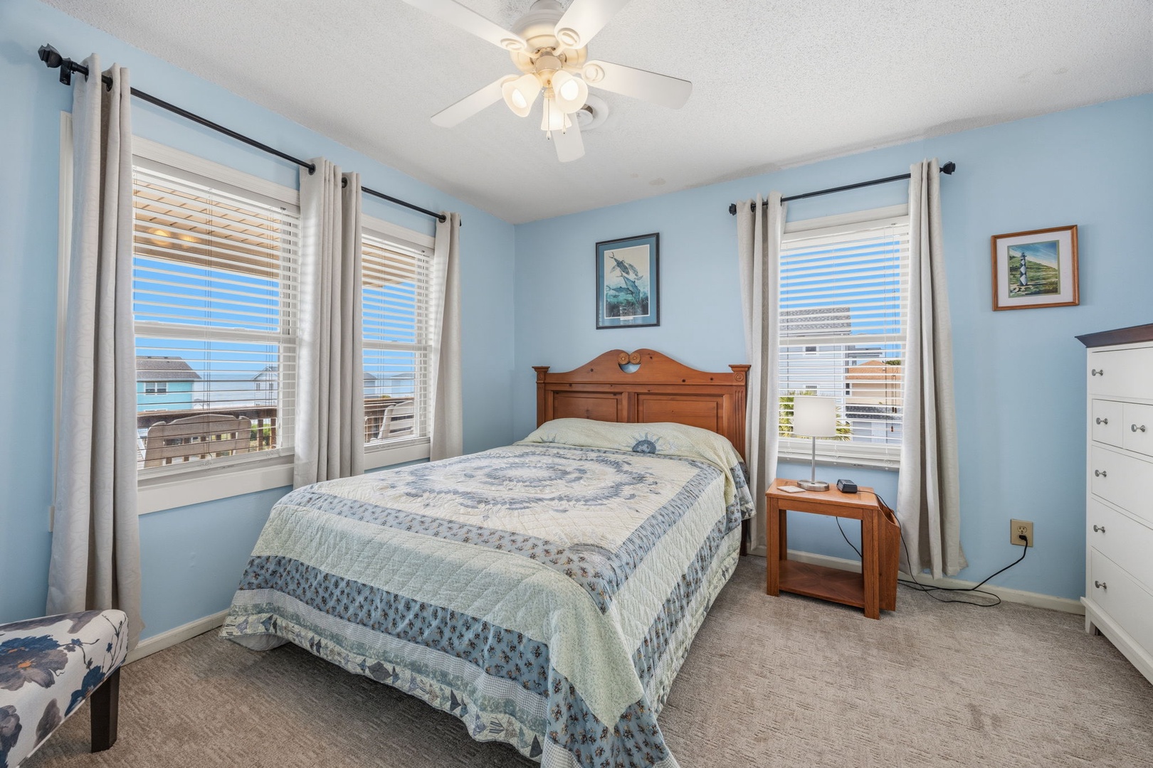 Drift off in your serene bedroom with soft blue walls, coastal artwork, and multiple windows bringing in natural light.