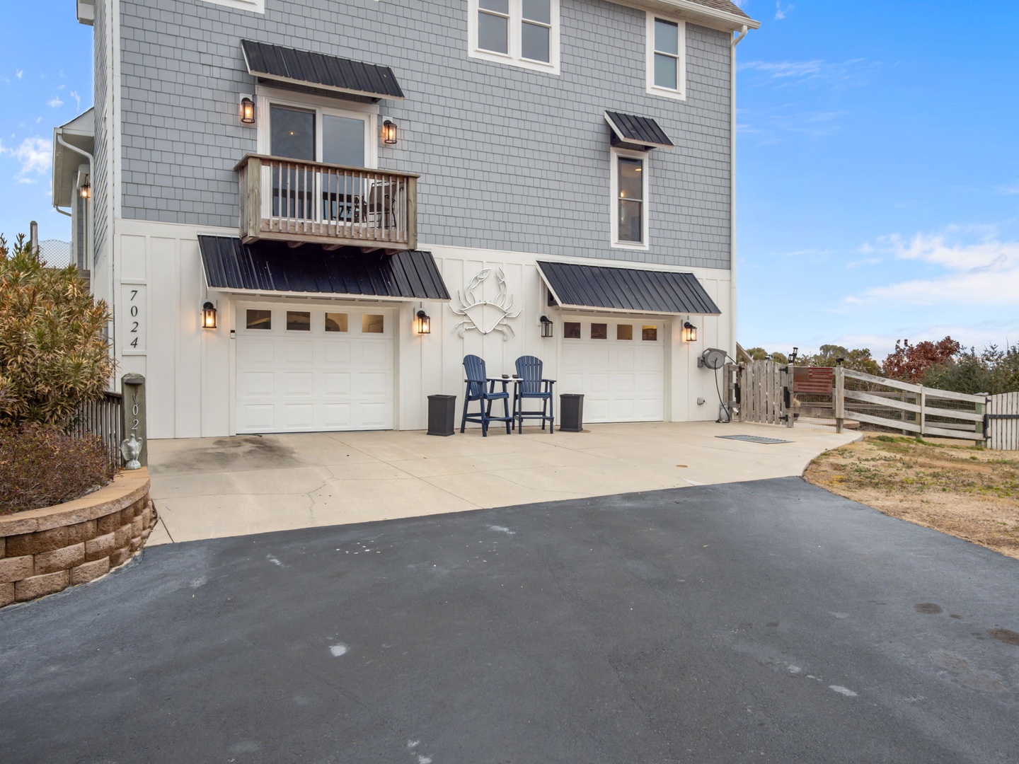 Coastal vacation home with gray shingles, private parking, and outdoor seating area under a bright blue sky.