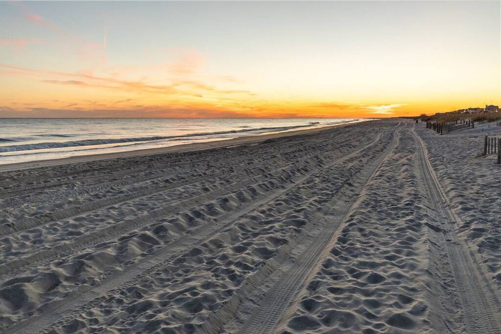 Pristine sandy beach stretches along the coastline with stunning sunset colors painting the sky in warm golden hues.