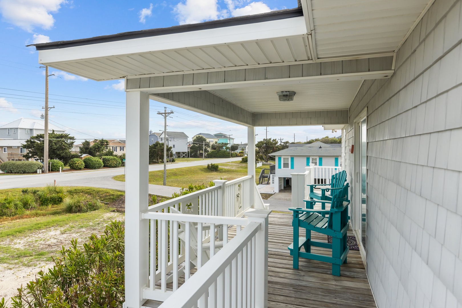 Covered porch with turquoise Adirondack chairs overlooks the peaceful neighborhood street and surrounding coastal community.