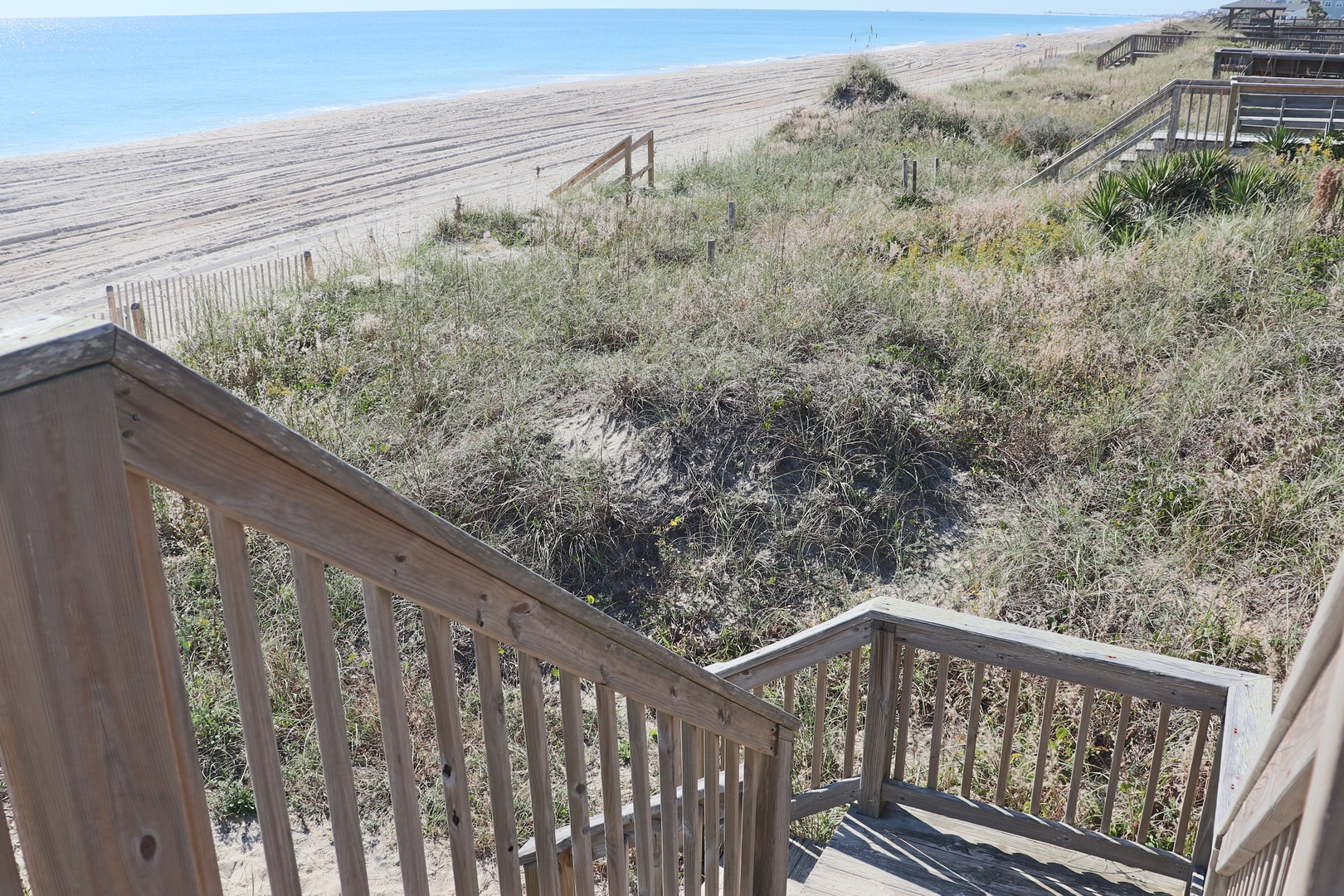 Wooden beach access stairs lead directly to pristine sandy shores with natural dune vegetation providing coastal charm.