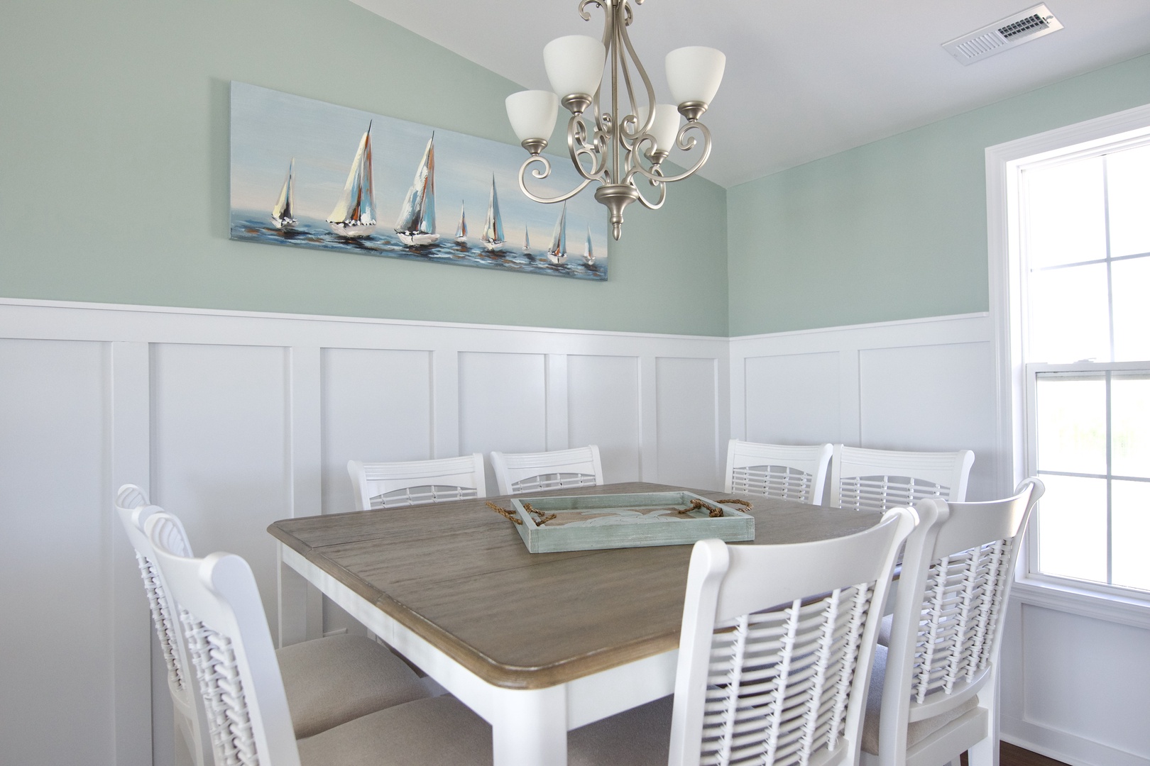 Gather around this inviting dining table where coastal charm meets comfort. The soft sea-green walls and nautical artwork create a serene atmosphere for your memorable meals together.