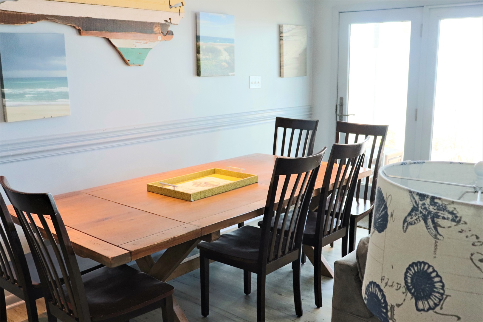 Gather around your spacious dining table for memorable meals, surrounded by coastal artwork and bright natural light streaming through French doors.