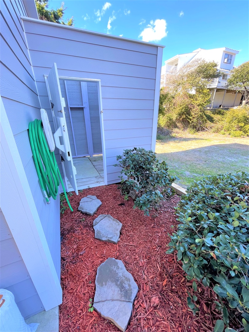 Outdoor shower awaits with garden hose and storage for beach gear after sunny days exploring.