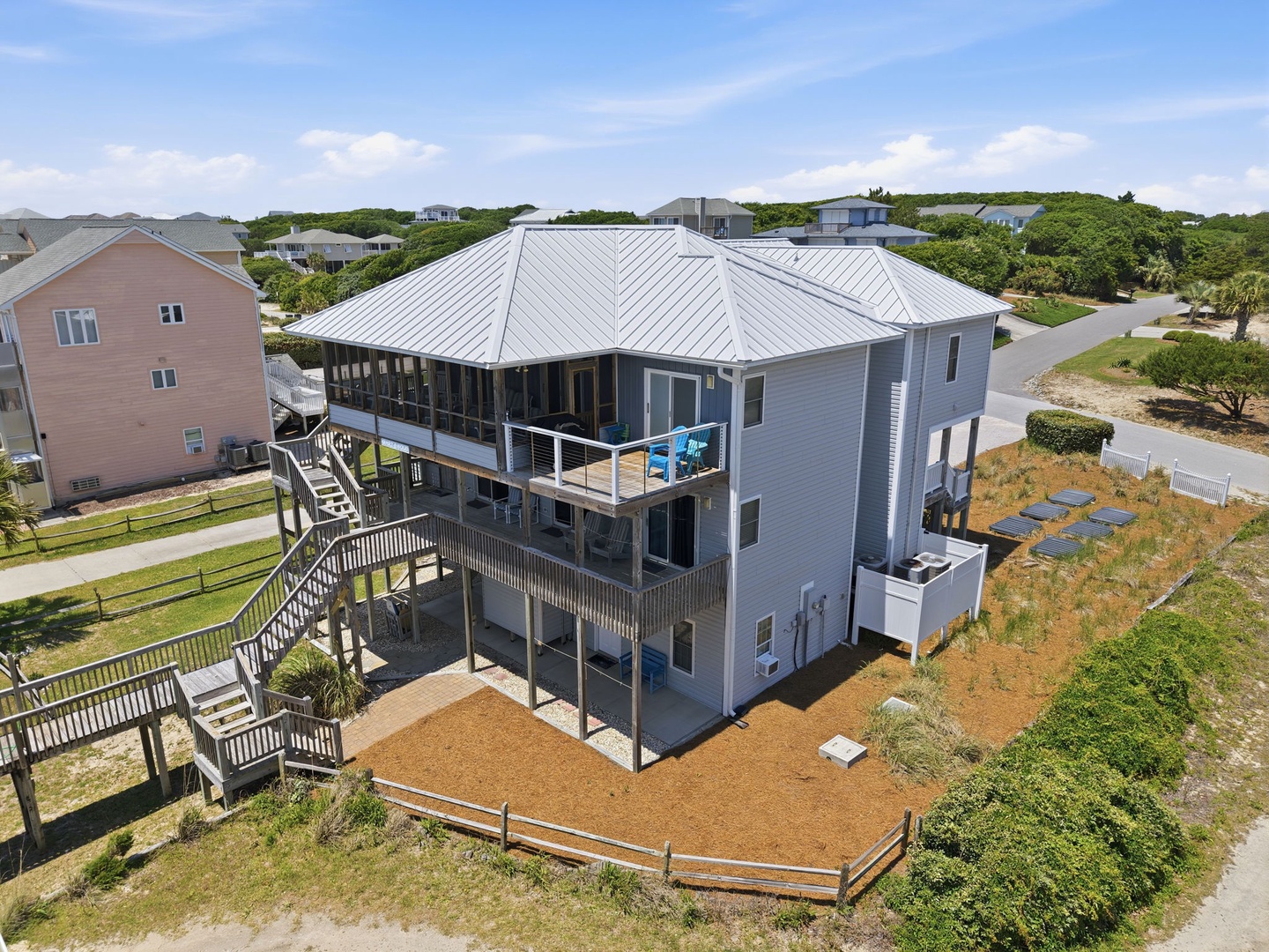 Aerial view of a spacious coastal vacation home featuring wraparound decks, beach access, and nestled in a residential area near the shore.