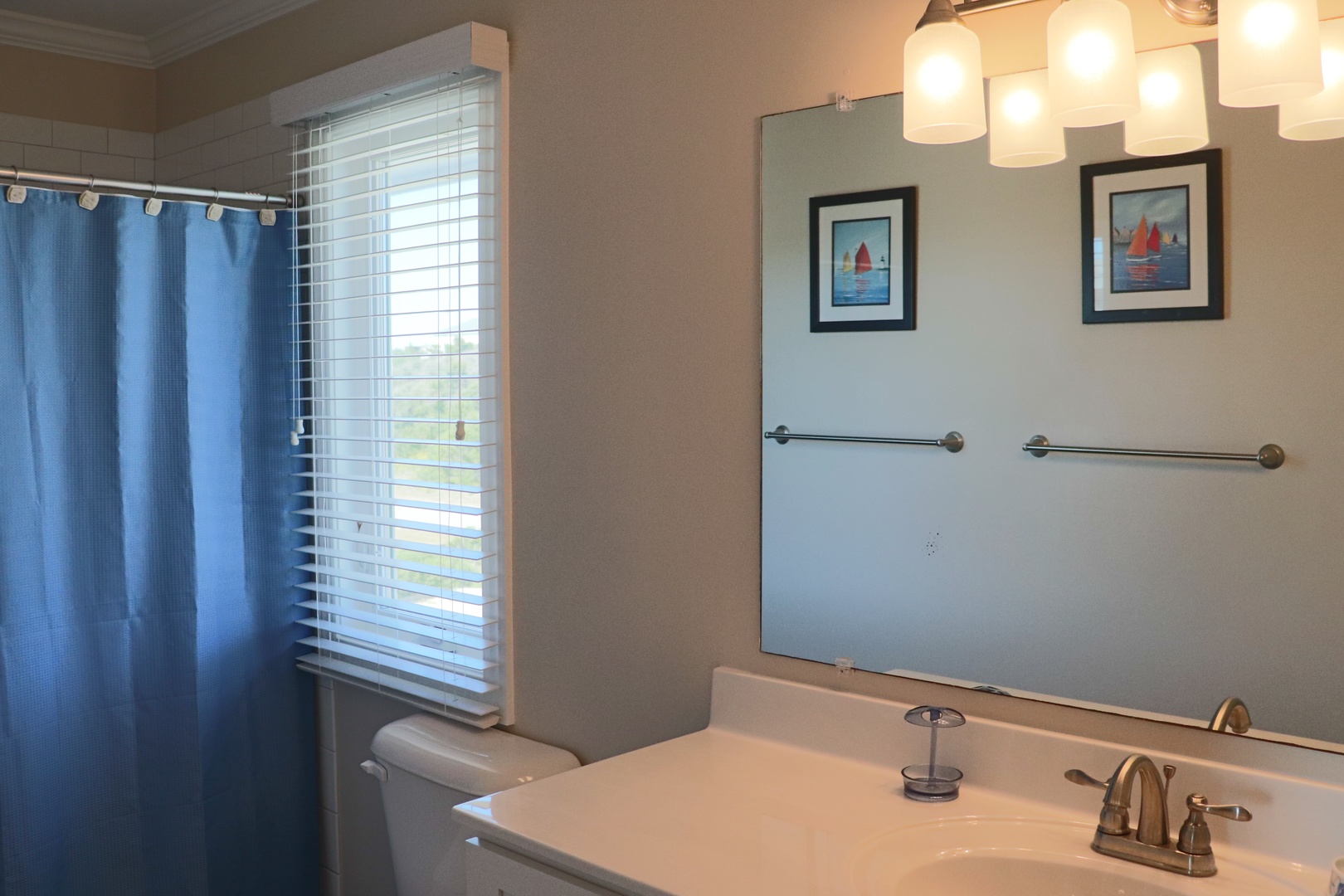 Refresh in your bright bathroom with modern fixtures, elegant lighting, and charming nautical artwork creating a welcoming coastal vibe.
