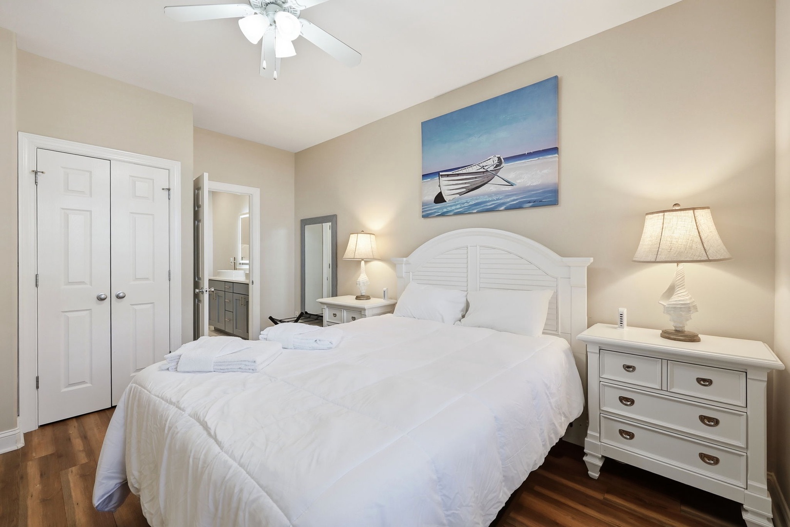 Sink into crisp white linens and unwind beneath soft lighting. Your peaceful coastal retreat awaits with charming nautical touches and a ceiling fan for comfort.