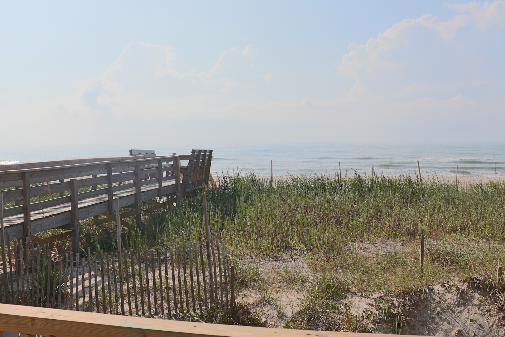 Coastal boardwalk leads to pristine sandy beach with ocean waves and natural dune grasses.
