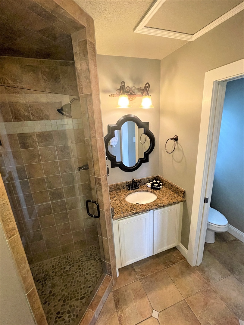 Unwind in your elegant bathroom featuring a stone-tiled shower, granite vanity, and stylish mirror for your daily refresh.