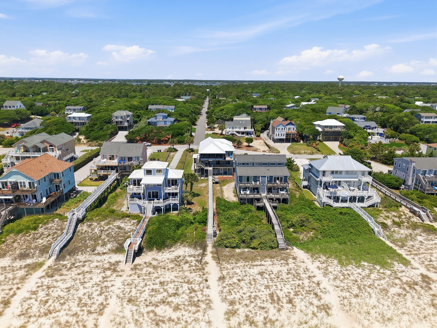 Aerial view of a coastal neighborhood with beachfront vacation homes featuring private access to sandy shores via wooden walkways.