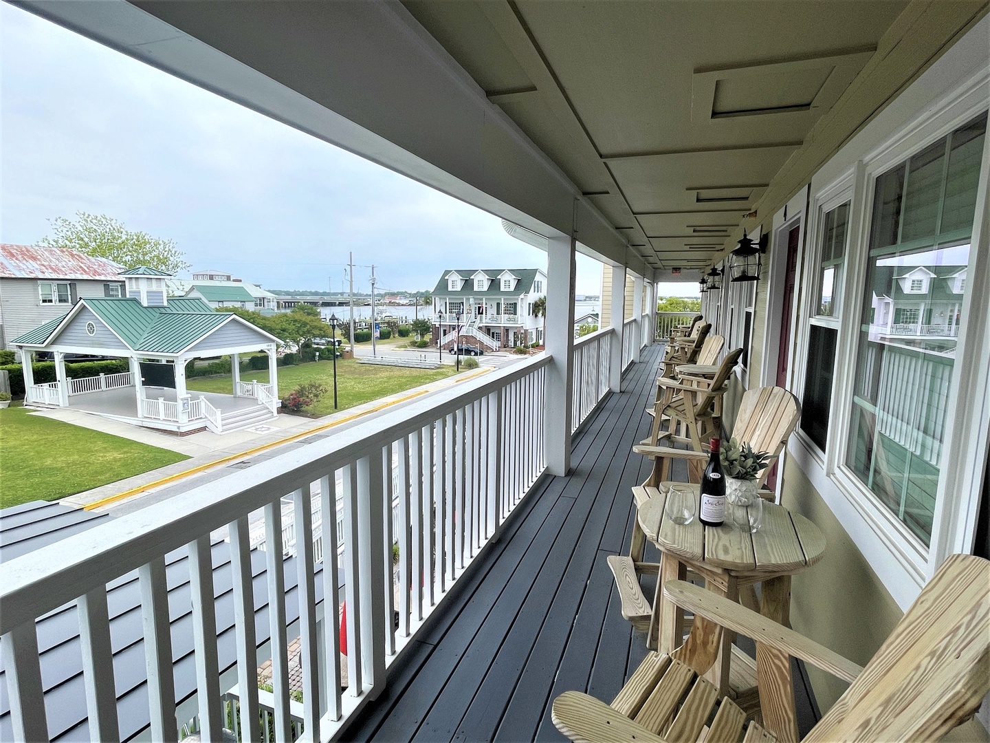 Expansive waterfront balcony with Adirondack chairs and small tables, perfect for enjoying coastal breezes and harbor views.