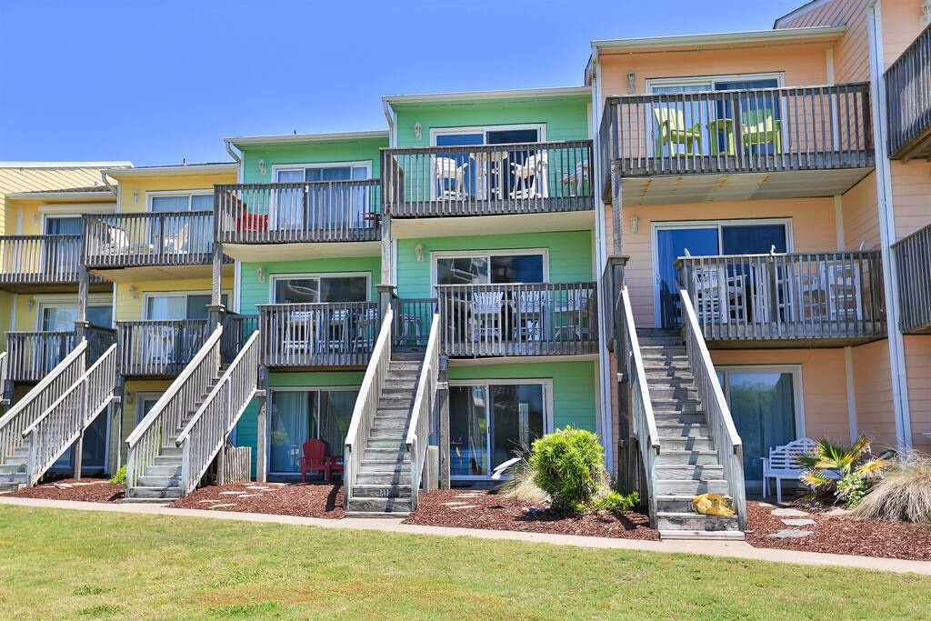 Vibrant beachfront townhomes with private balconies and direct beach access via wooden stairs.