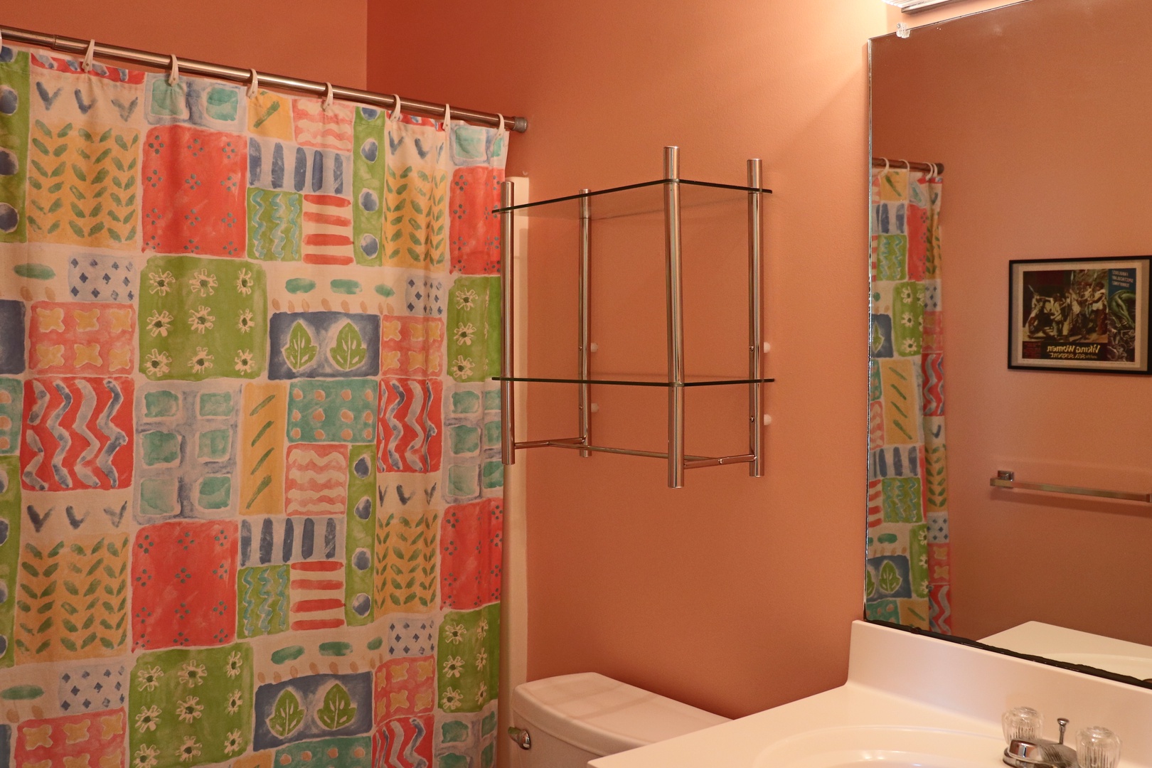 Freshen up in your vibrant bathroom featuring cheerful patchwork shower curtain and warm coral walls that create a welcoming atmosphere.