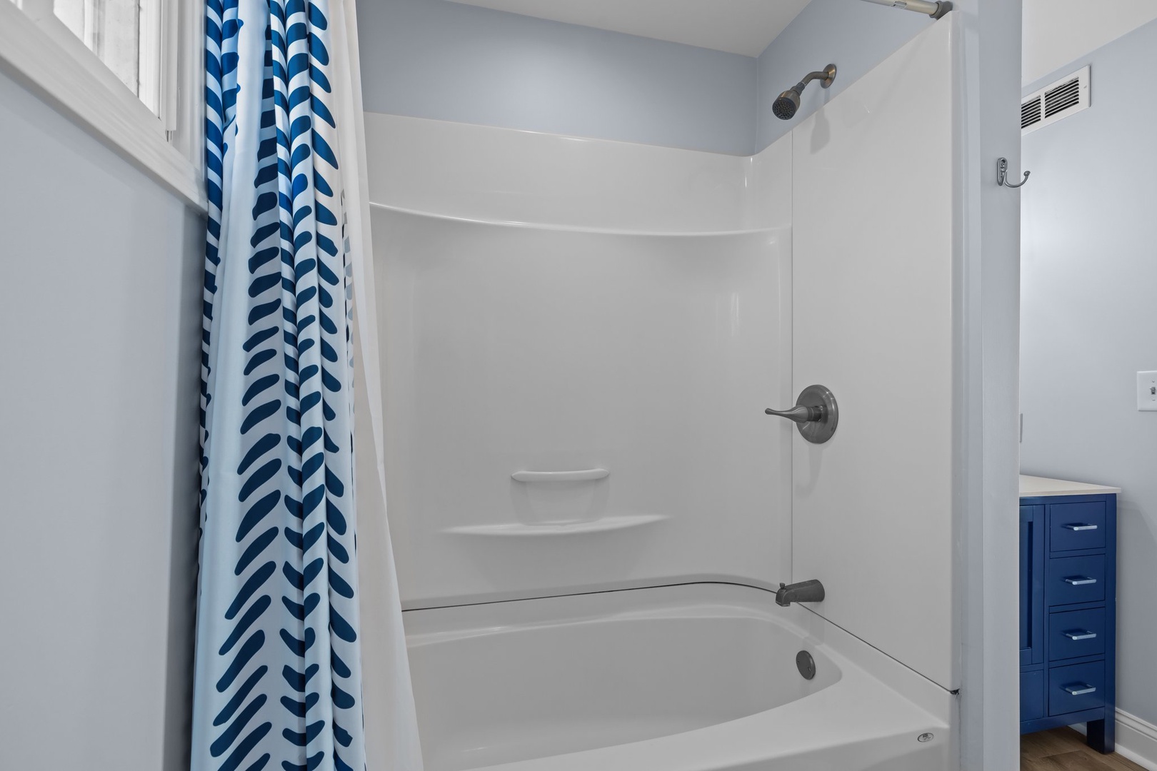 Step into your pristine bathroom featuring a spacious tub-shower combo with cheerful blue chevron curtains and modern fixtures for relaxing soaks.
