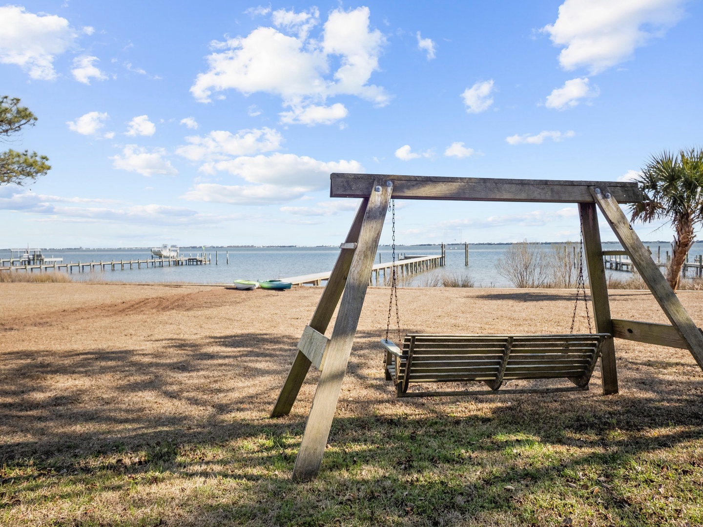 Peaceful waterfront setting with wooden swing overlooking calm bay waters and distant pier structures.