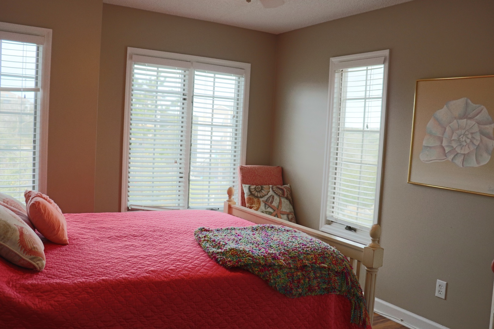 Sink into your cozy corner bedroom where vibrant coral bedding and soft natural light create the perfect retreat for restful nights.