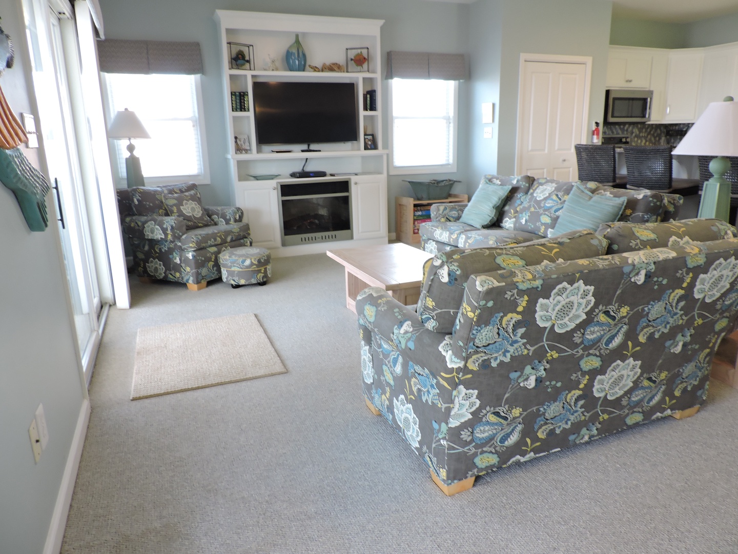 Settle into your cozy living space with soft floral seating, built-in entertainment center, and bright windows creating the perfect retreat for relaxation.