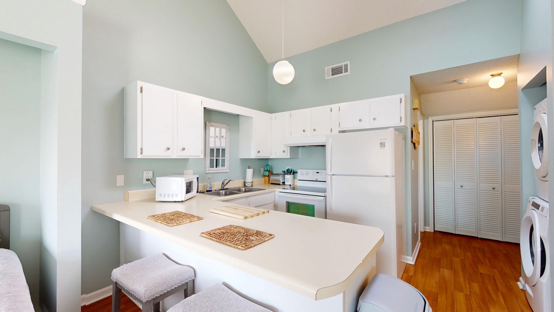 Your fully equipped kitchen features white cabinets, modern appliances, and a breakfast bar where you can enjoy morning coffee in the soothing mint-green space.