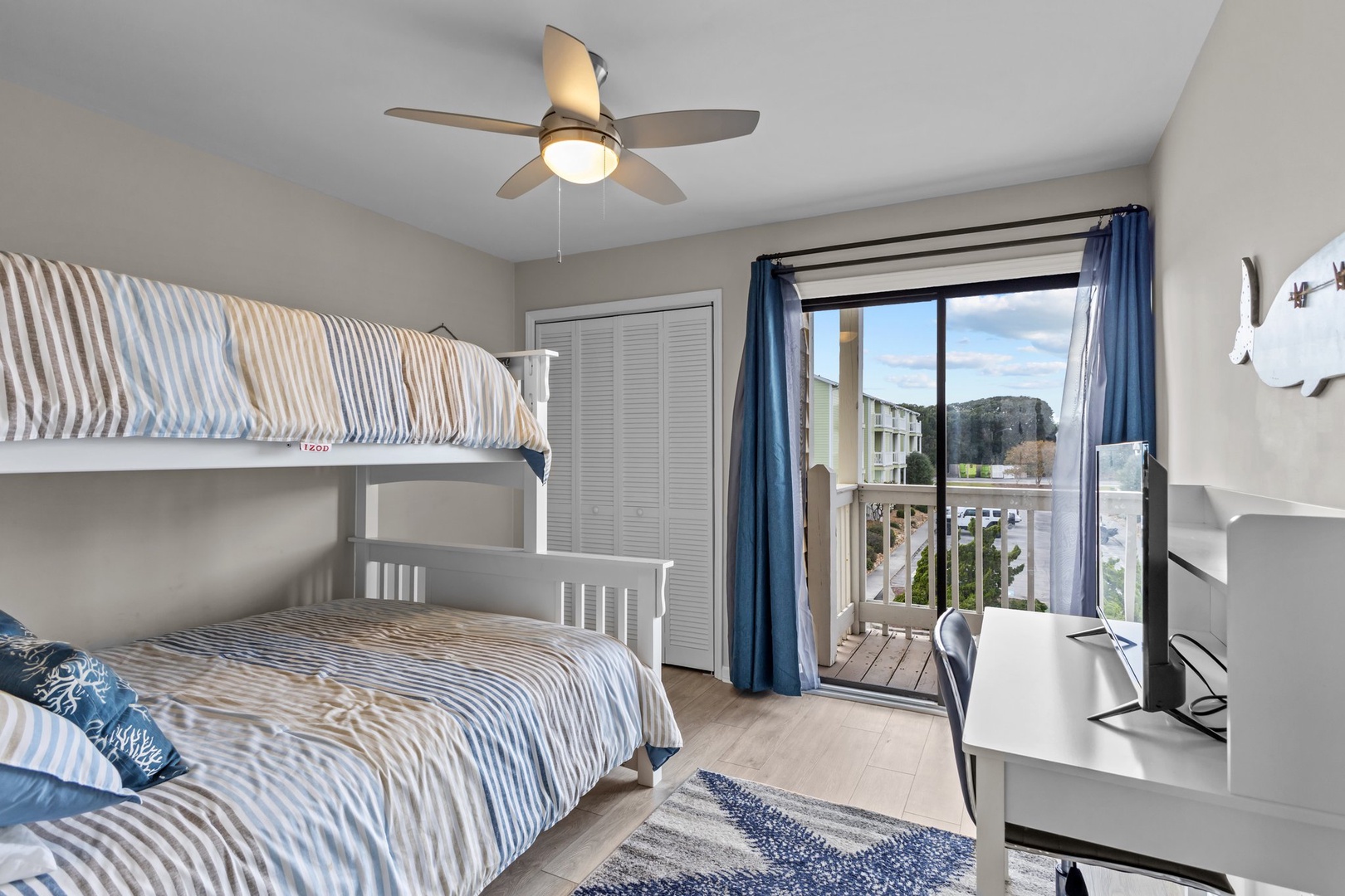 Your coastal bedroom features bunk beds with ocean-blue linens, a private balcony, and fresh sea breezes from the ceiling fan overhead.
