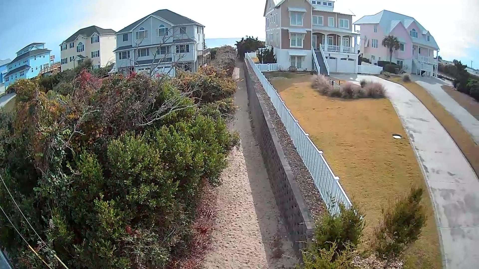 Elevated view of colorful beachfront homes in a coastal residential neighborhood with sandy pathways and natural vegetation.