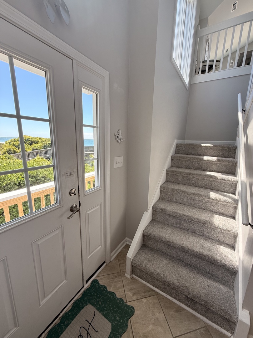 Step into your bright, airy entryway with plush carpeted stairs and elegant white doors welcoming you home. Sunshine spills through tall windows, setting a warm, inviting tone for your stay.