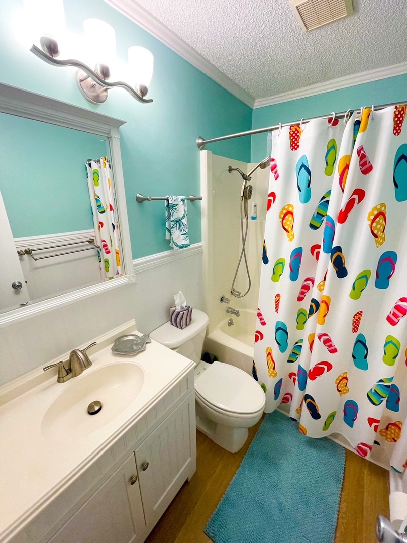Step into your cheerful beach-themed bathroom with colorful flip-flop curtain and soothing turquoise walls perfect for freshening up after sandy adventures.