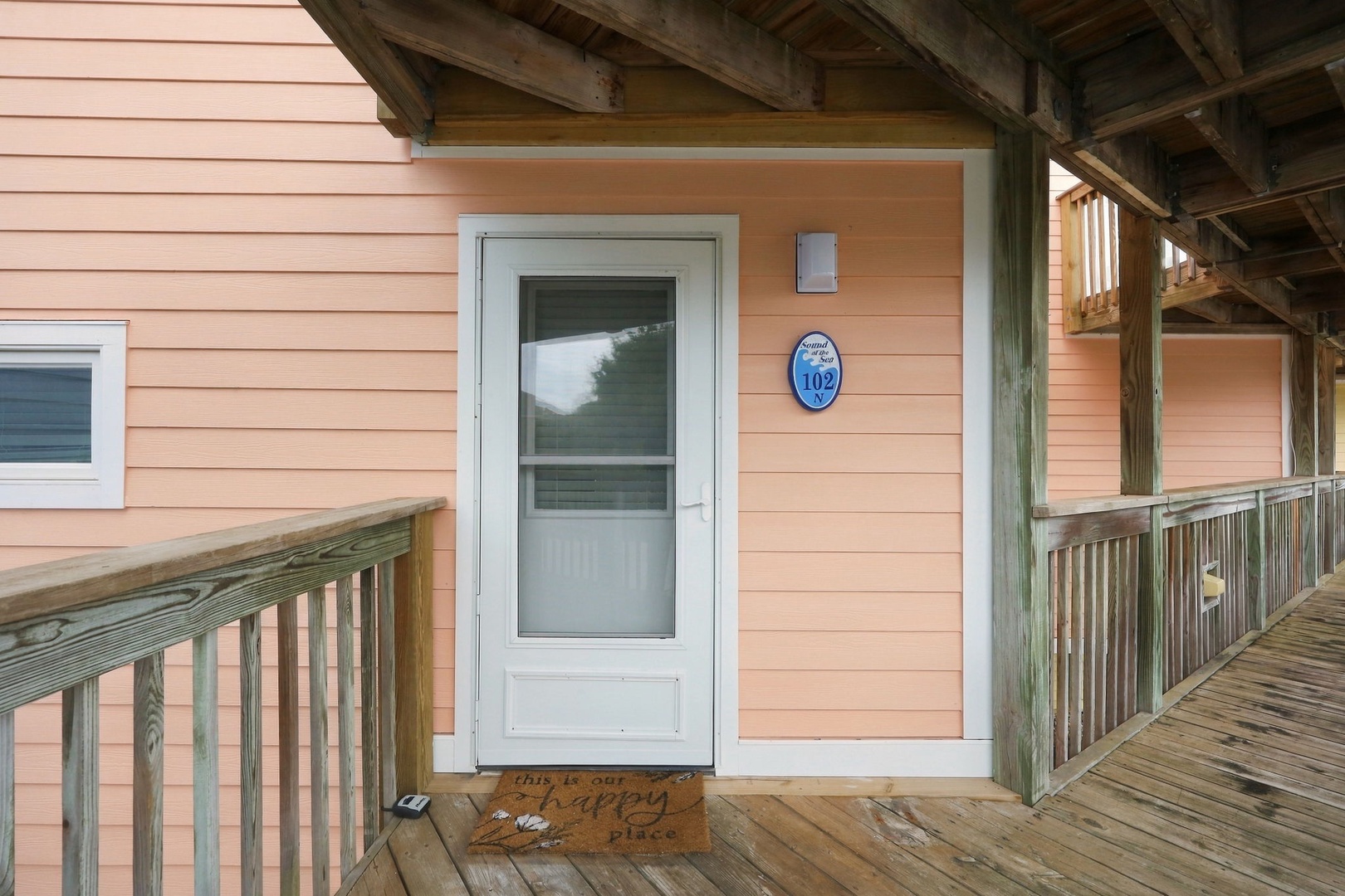 The entrance to unit 102 features a welcoming covered walkway with rustic wooden posts and a charming peach exterior, ready for your arrival.