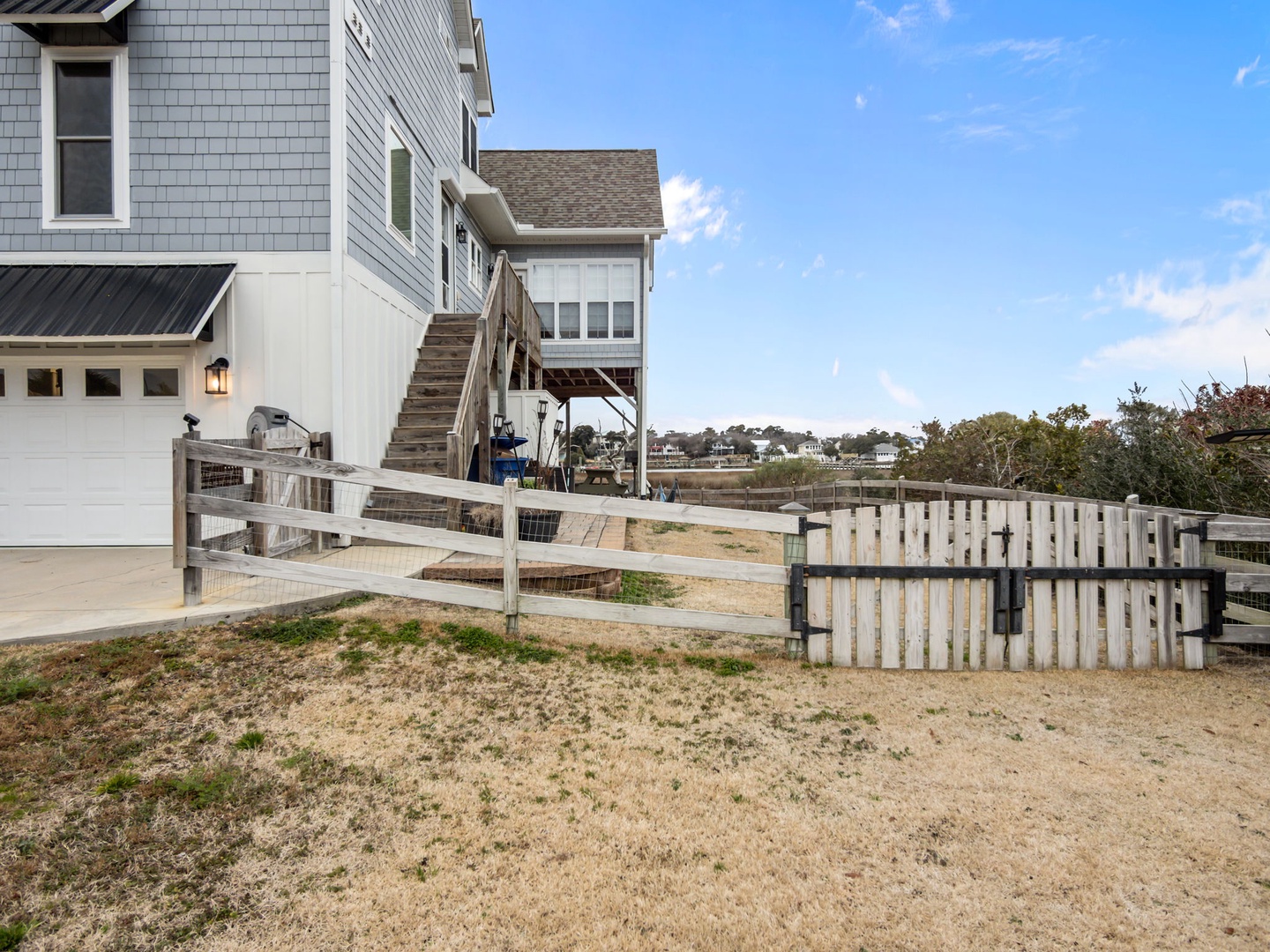 Coastal property exterior with modern beach house design and wooden fence enclosing private yard area under clear blue skies.