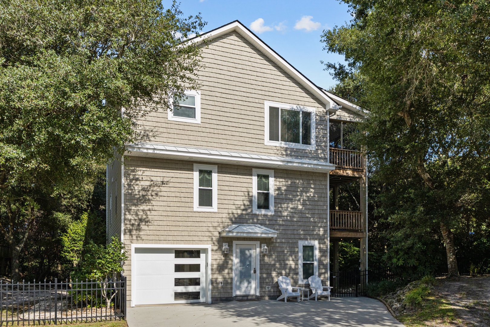 A charming three-story coastal home nestled among mature trees, featuring natural shingle siding and welcoming front entrance with seating area.