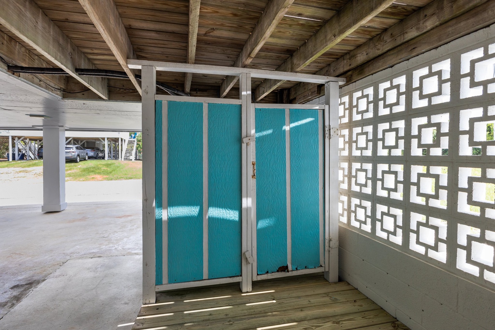 Step into your private outdoor shower space, where tropical turquoise panels and decorative screens create a refreshing retreat beneath rustic wooden beams.
