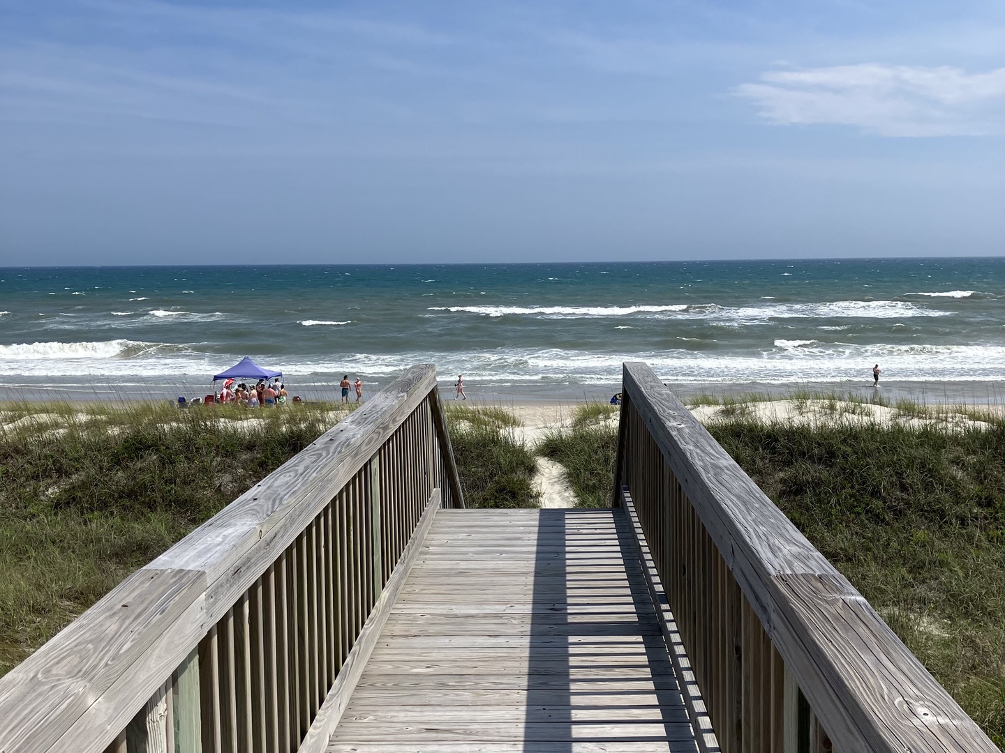 Wooden boardwalk leads directly to pristine sandy beach with rolling waves and coastal dunes nearby.