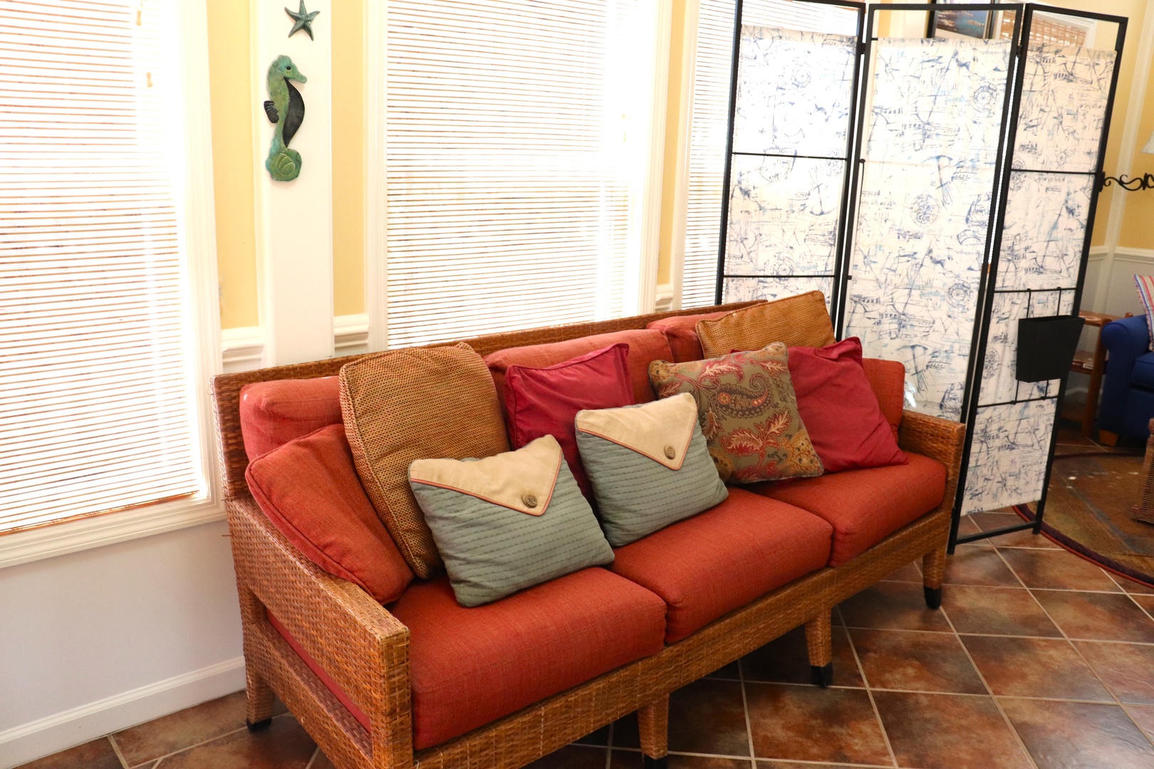 Unwind on your private wicker sofa with ocean-themed decor, where colorful cushions invite relaxation by sunlit windows.