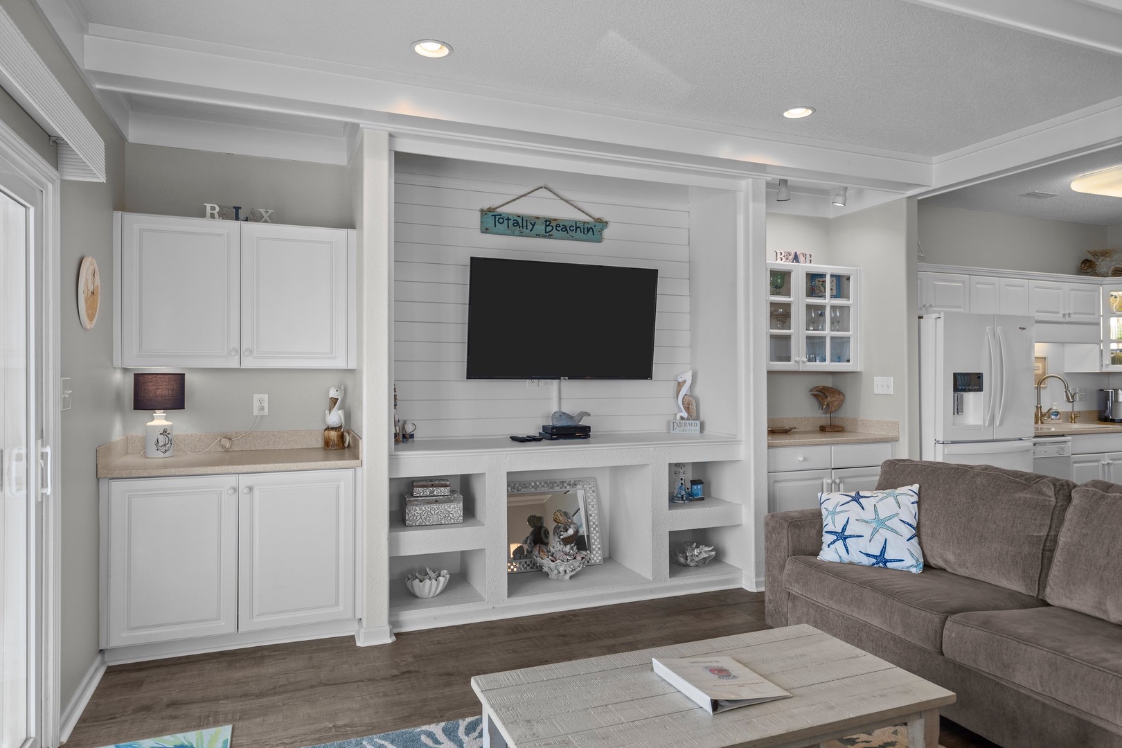 Relax in your coastal living space with built-in entertainment center, custom cabinetry, and charming beach-themed decor.