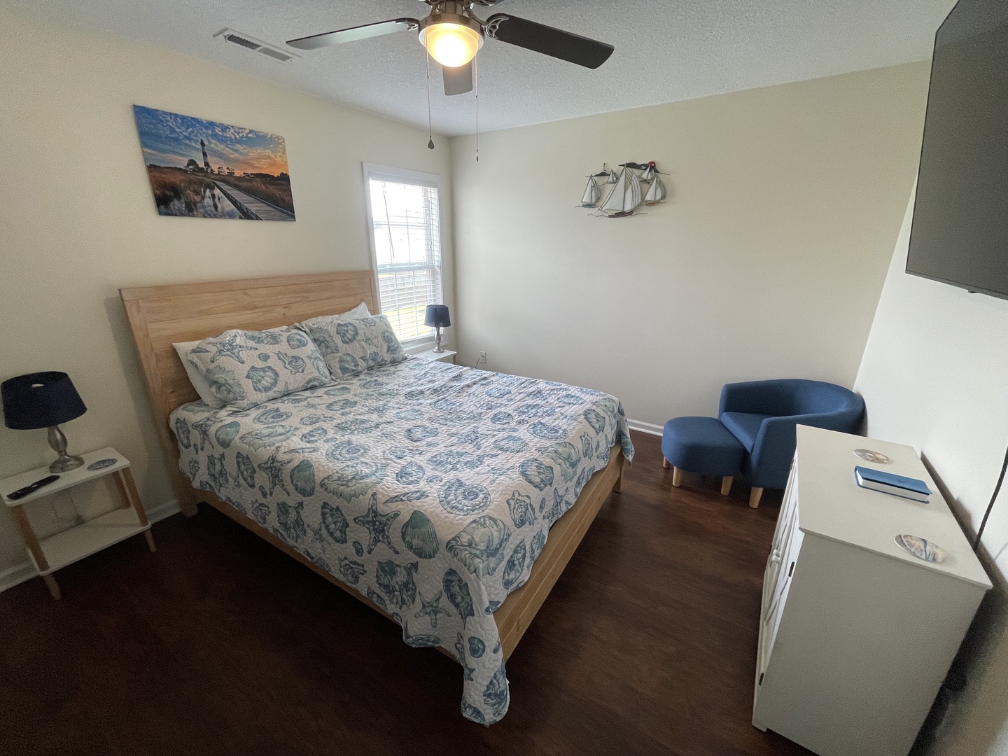 Unwind in your peaceful bedroom with a comfortable queen bed, ceiling fan, and cozy blue chair for relaxing.