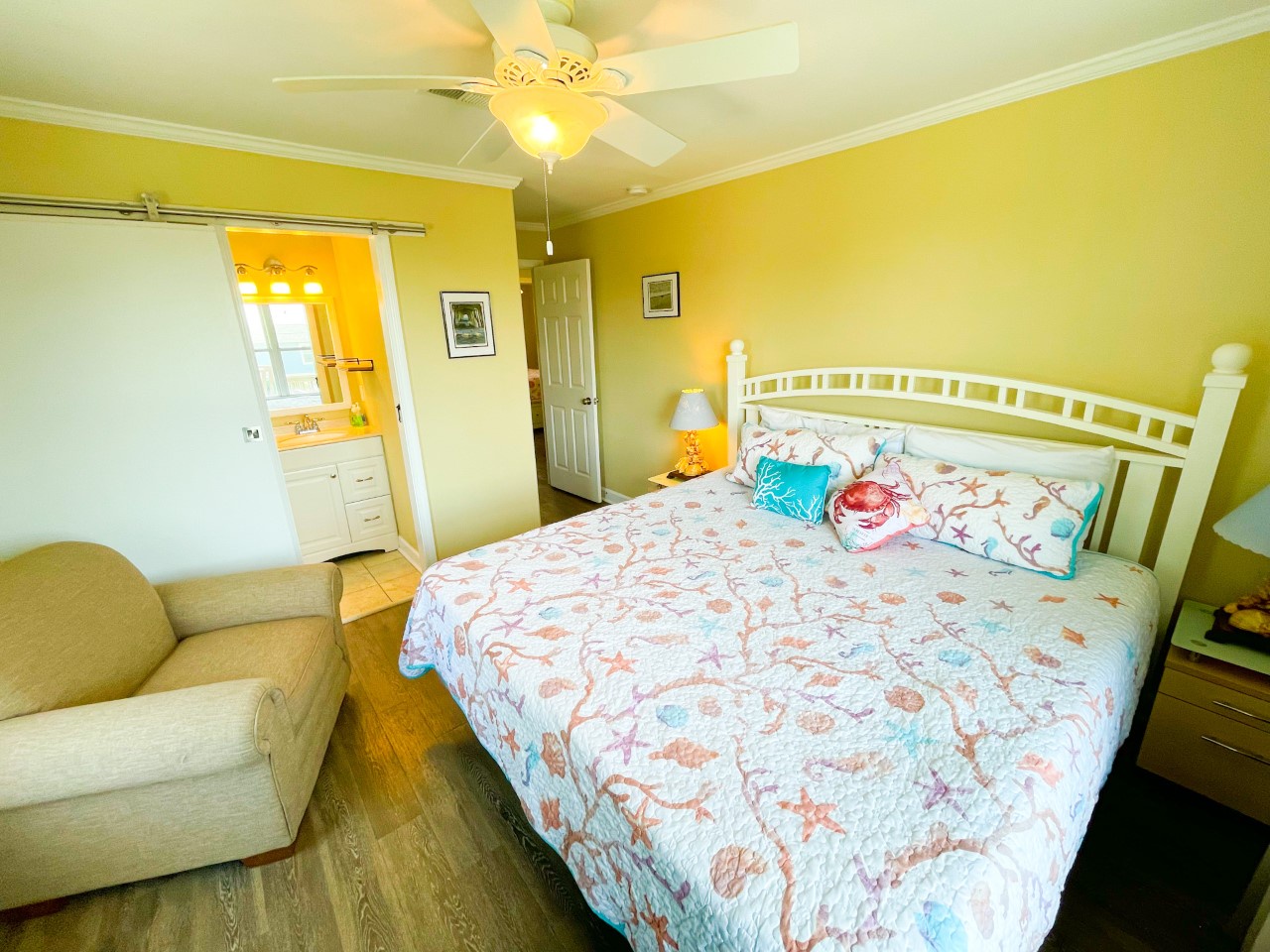 Relax in your bright, cheerful bedroom with ocean-themed bedding and cozy seating area, complete with ceiling fan and en-suite access.