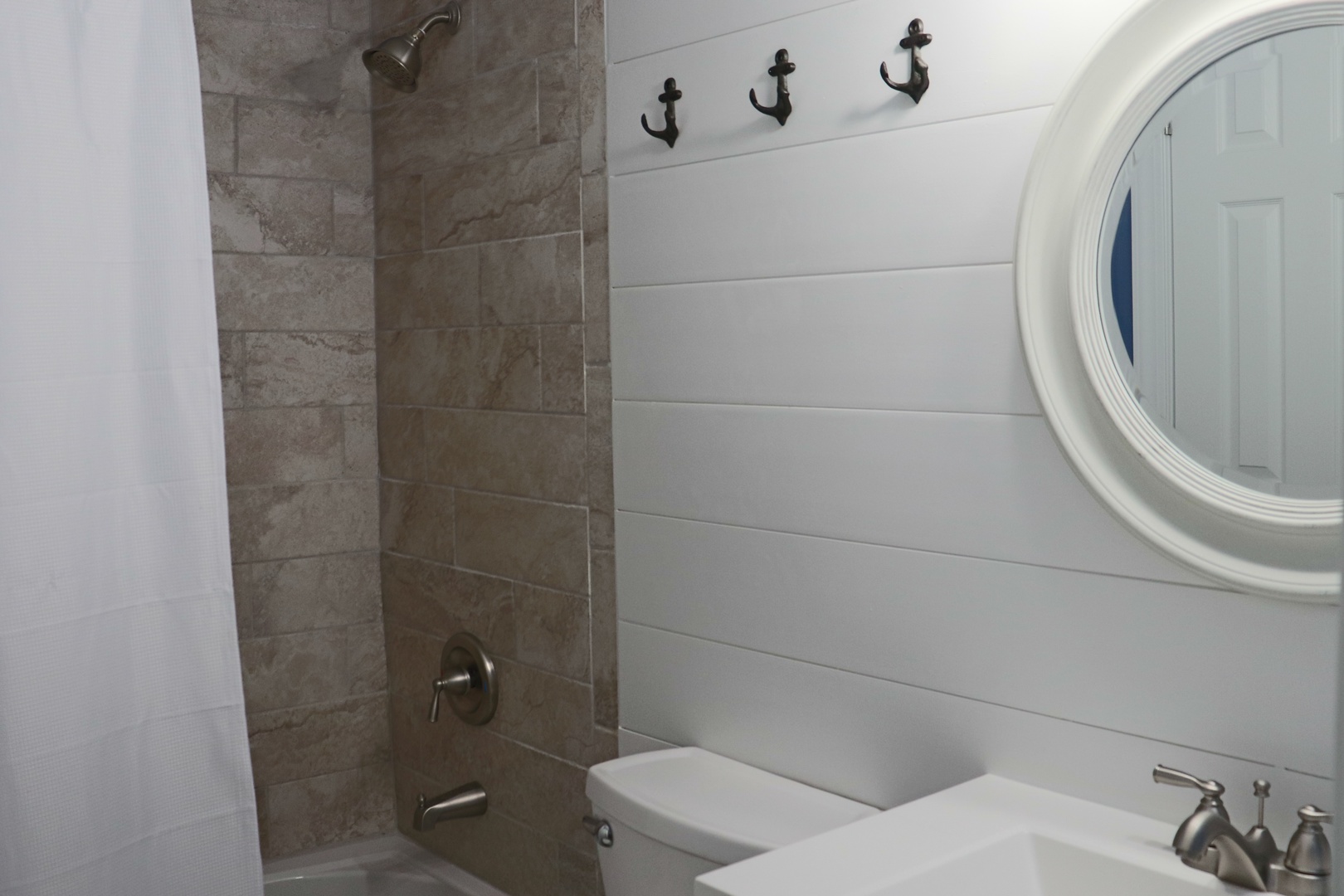 Refresh in your coastal-themed bathroom with stylish anchor hooks and a luxurious stone-tiled shower.