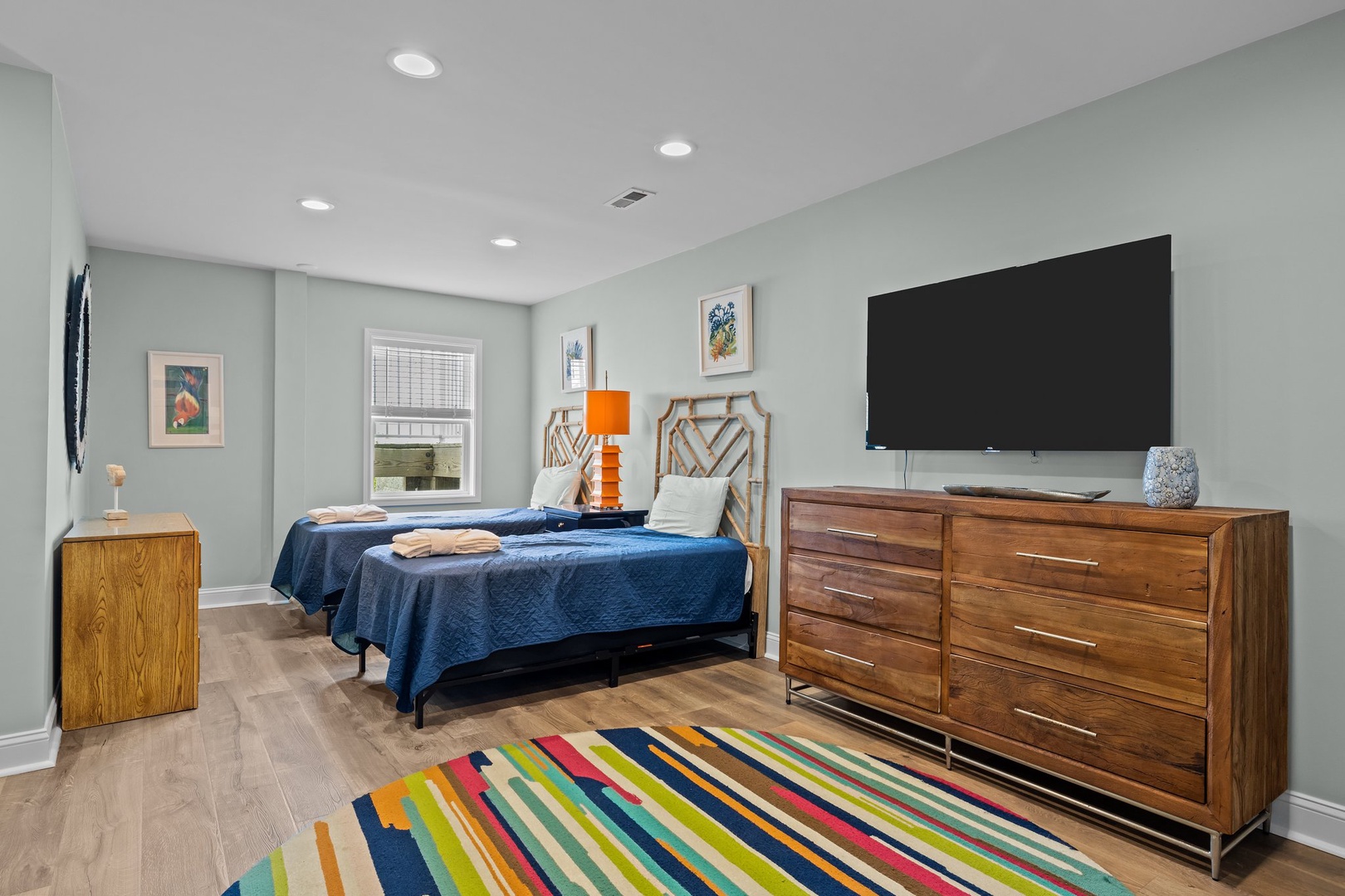 Relax in your modern bedroom featuring twin beds with cozy navy linens and vibrant striped rug adding warmth.