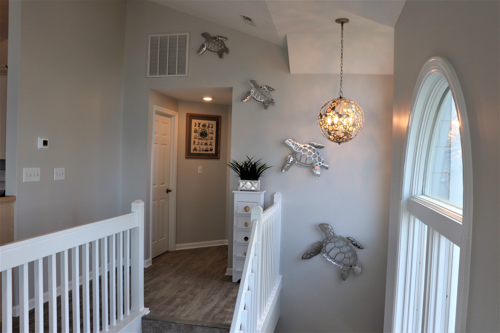 Your upstairs hallway welcomes you with charming sea turtle art and warm pendant lighting, creating a coastal haven that feels like home.
