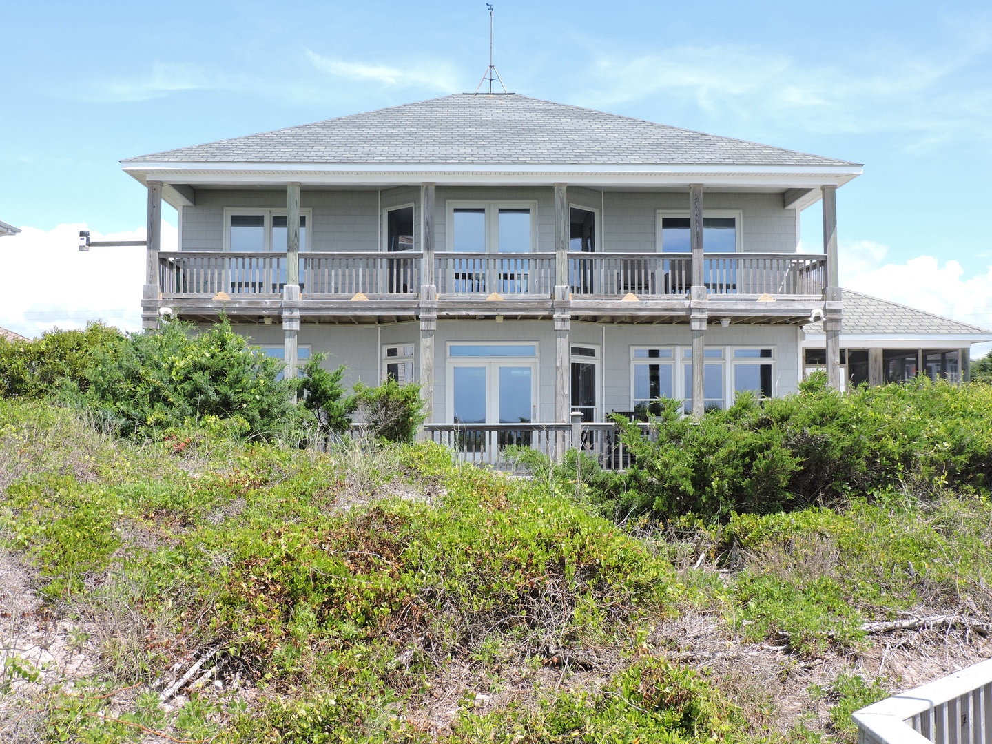 Charming two-story coastal home with wraparound balconies nestled among natural dunes and native vegetation.