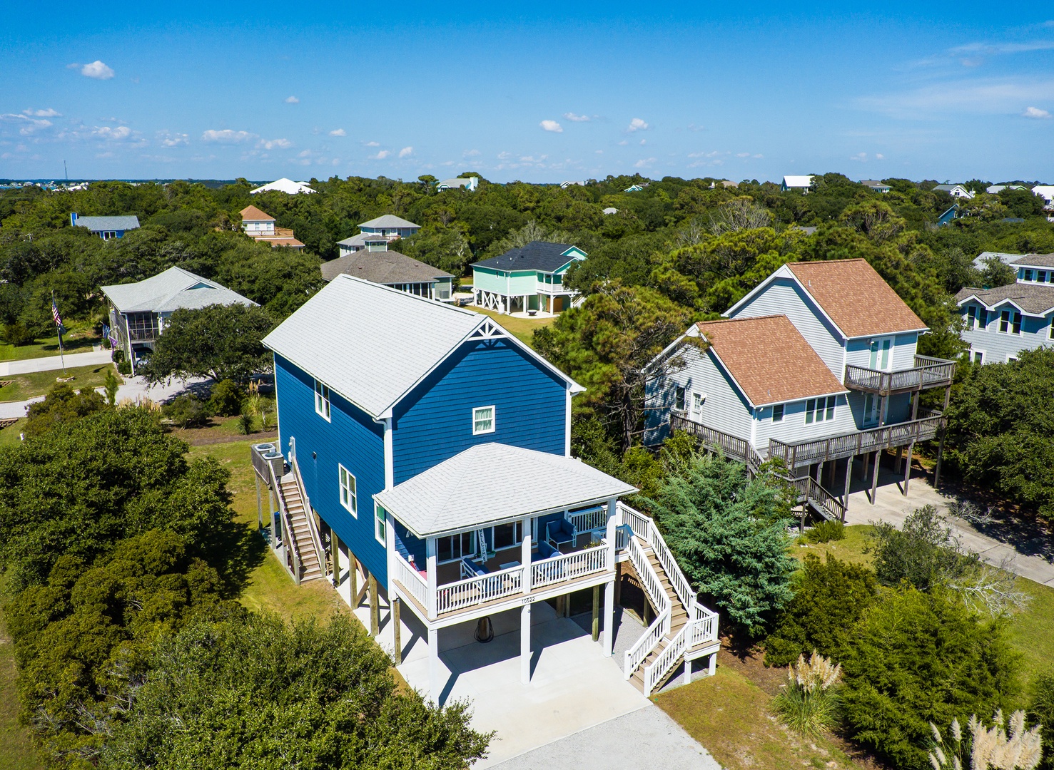 Charming blue beach house nestled among coastal trees in a peaceful residential neighborhood with convenient parking and elevated deck access.