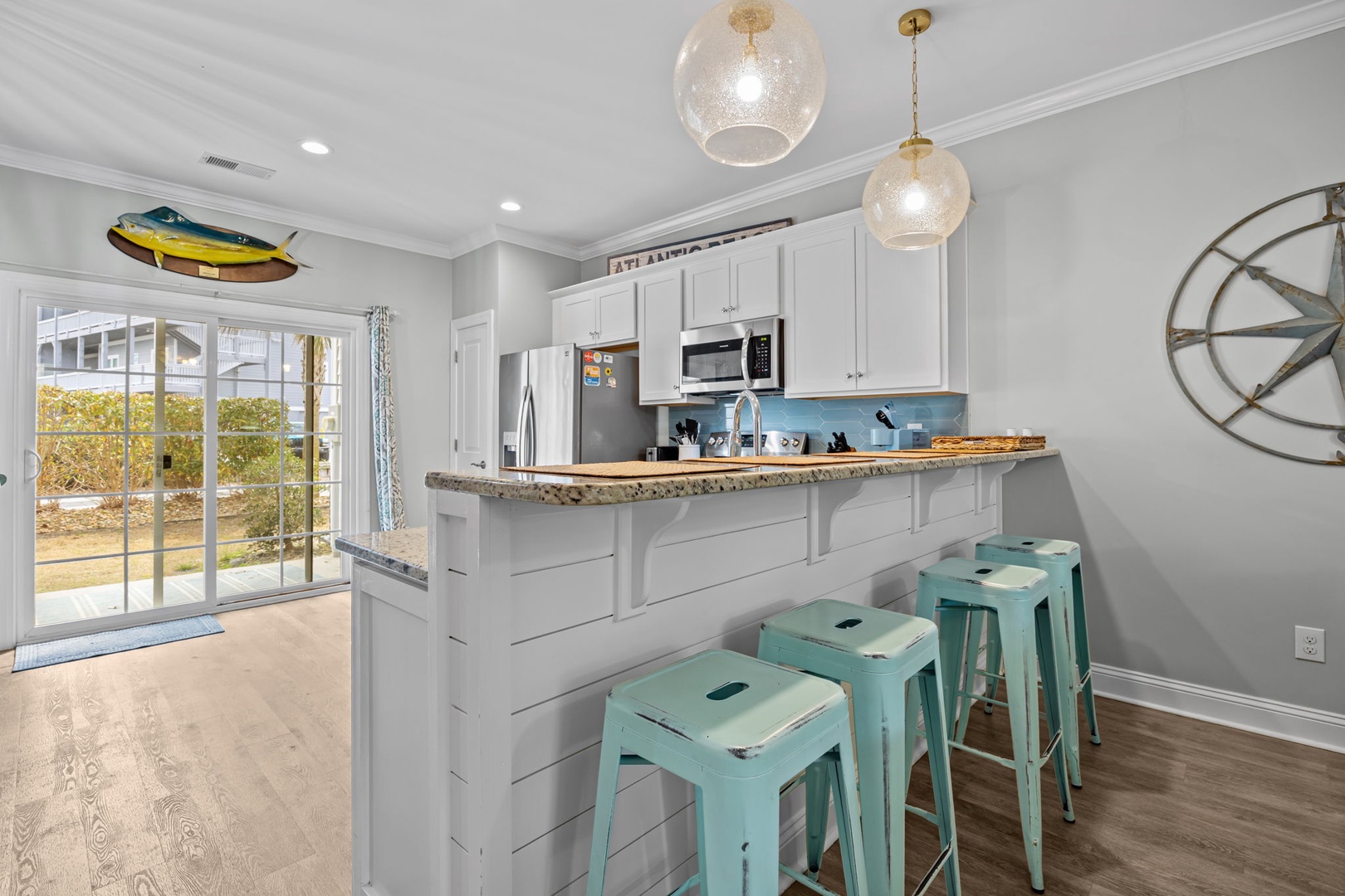 Your coastal-inspired kitchen features white cabinets, granite countertops, and charming turquoise bar stools perfect for morning coffee or casual meals together.