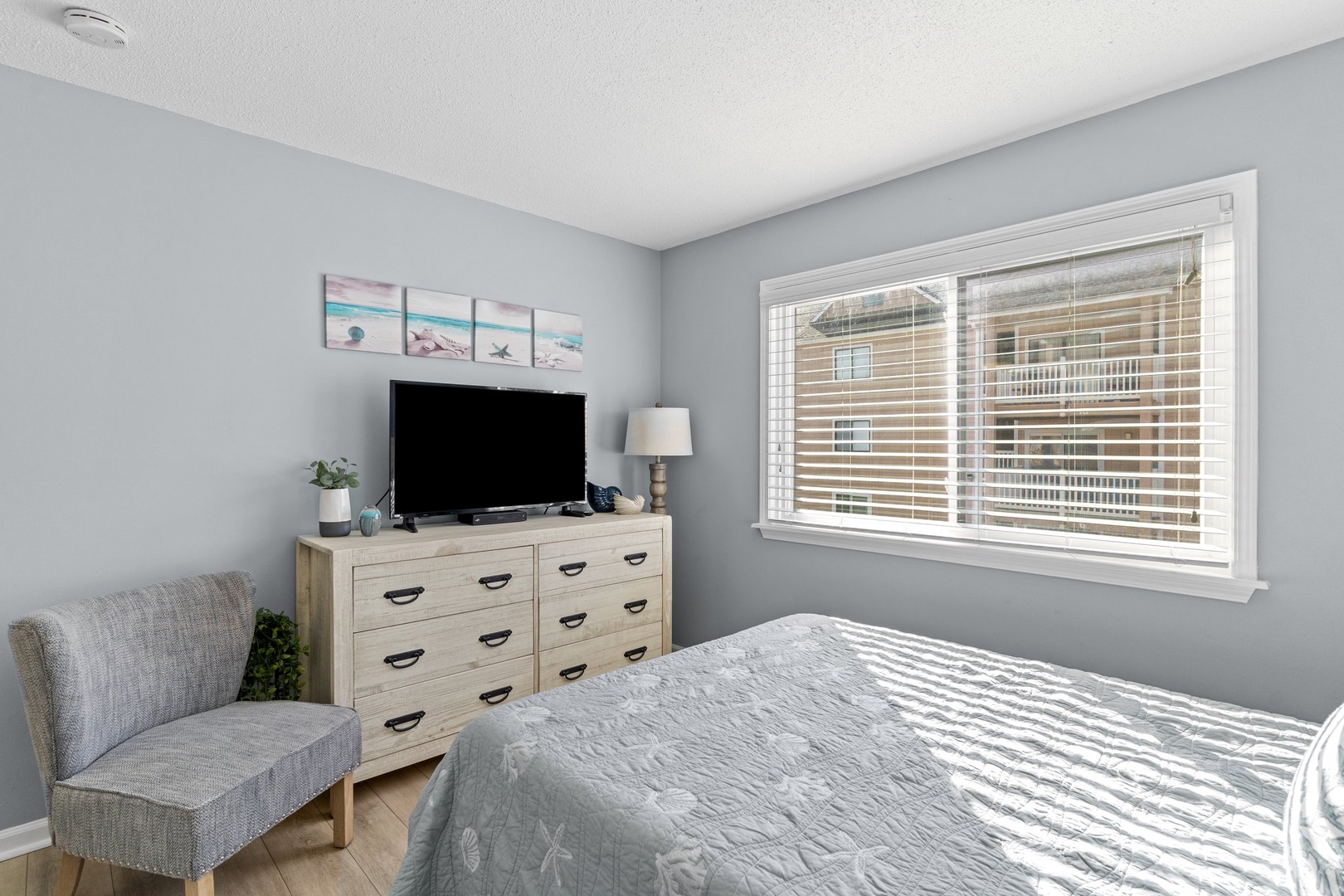 Unwind in your peaceful bedroom with modern furnishings, smart TV entertainment, and natural light streaming through venetian blinds.