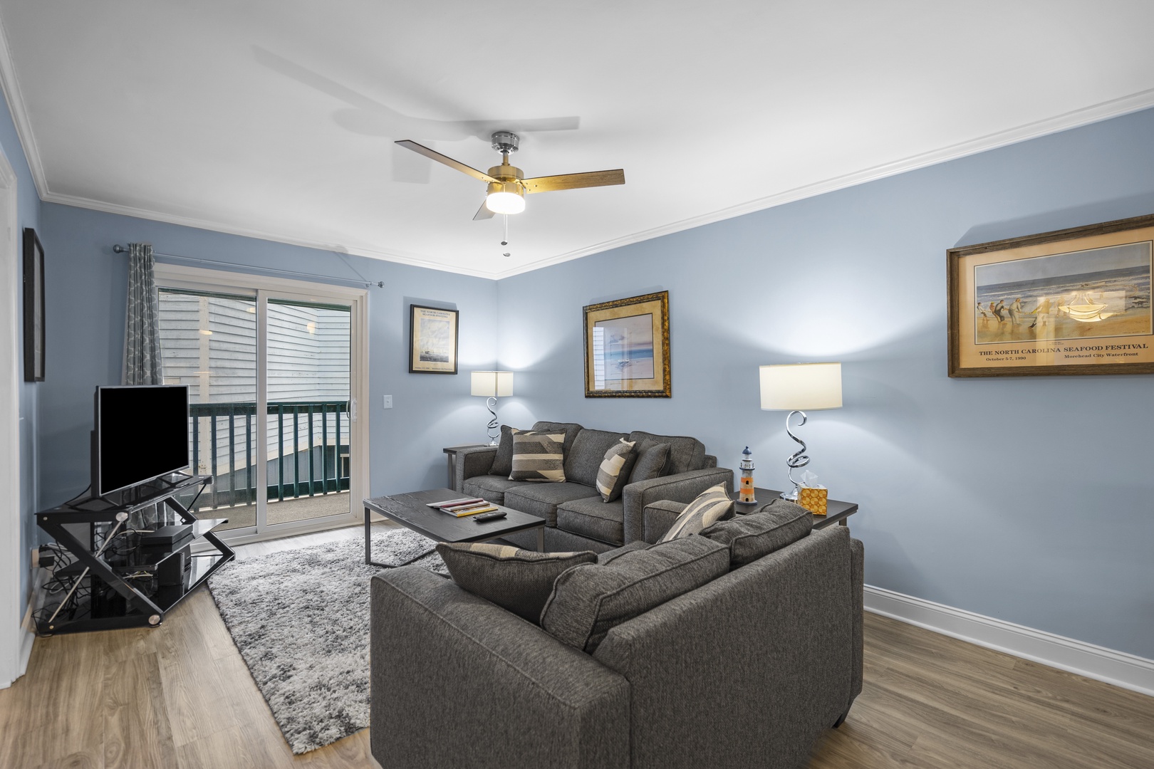 Relax in your comfortable living room with ceiling fan, modern TV setup, and access to your private balcony.